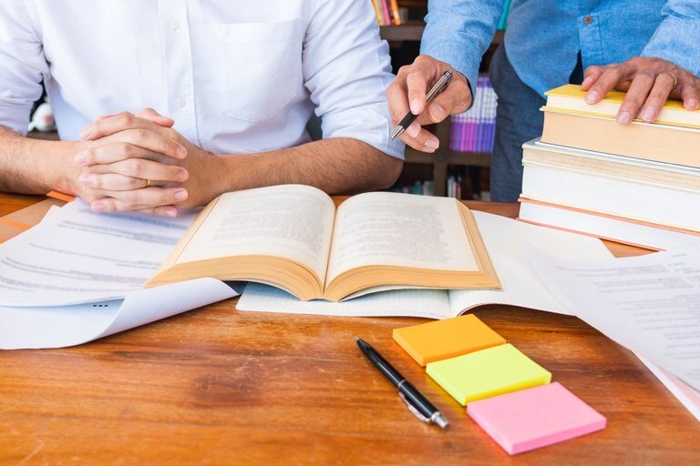 Eine Wissenschaftlerin und ein Wissenschaftler arbeiten hinter einer Glasfassade und mischen Chemikalien mit Großgeräten.
